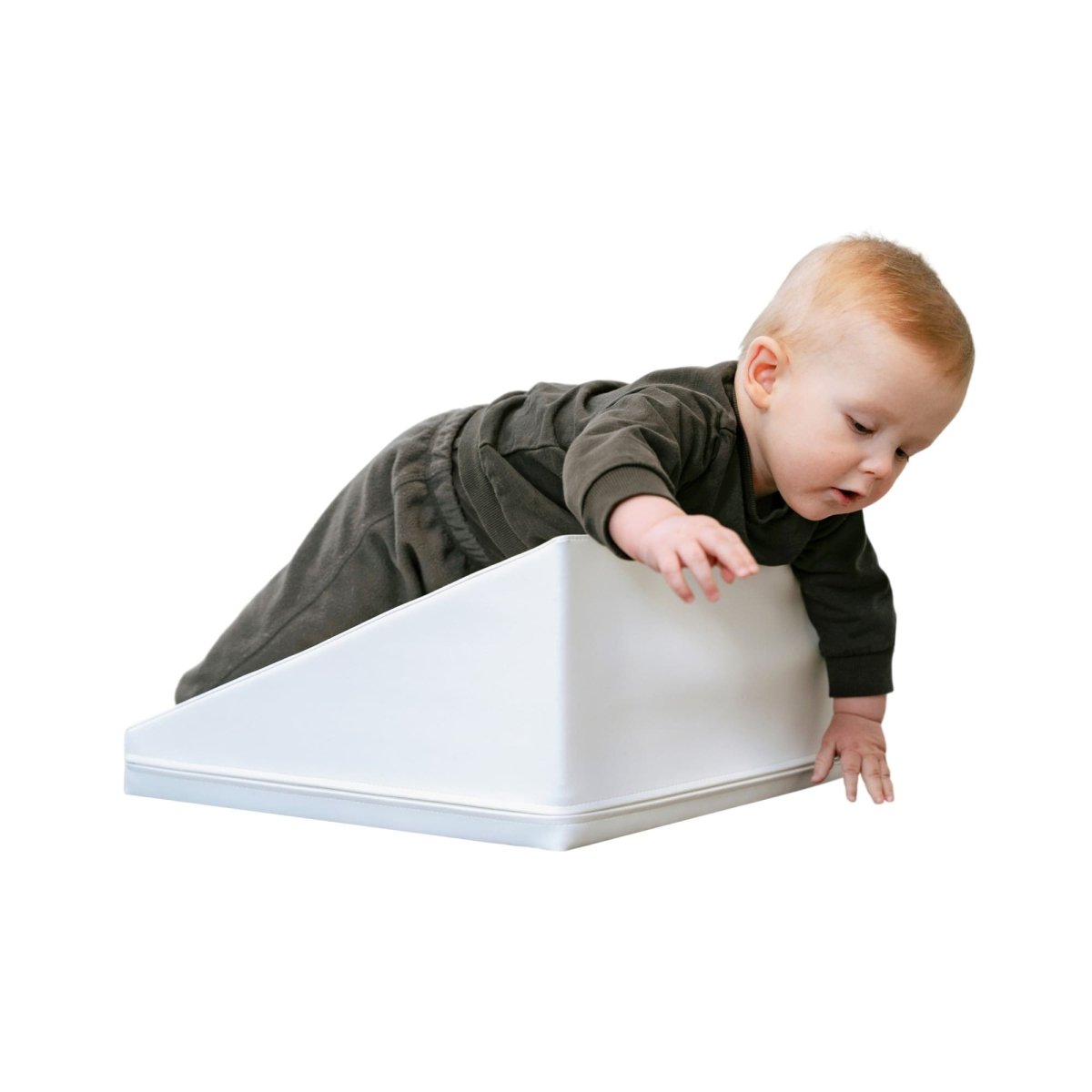 A baby in a dark outfit climbs a white, soft foam ramp, slightly balancing with their left arm