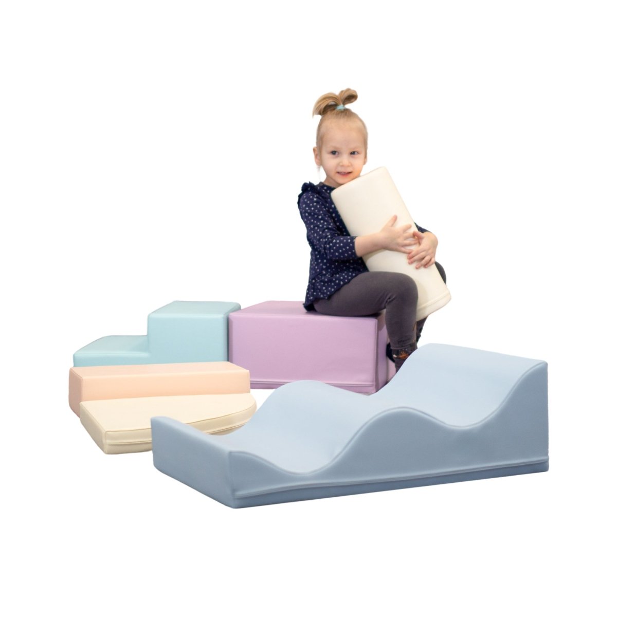 A smiling girl sits on a pastel multicolored soft play set, hugging a white cylinder shape