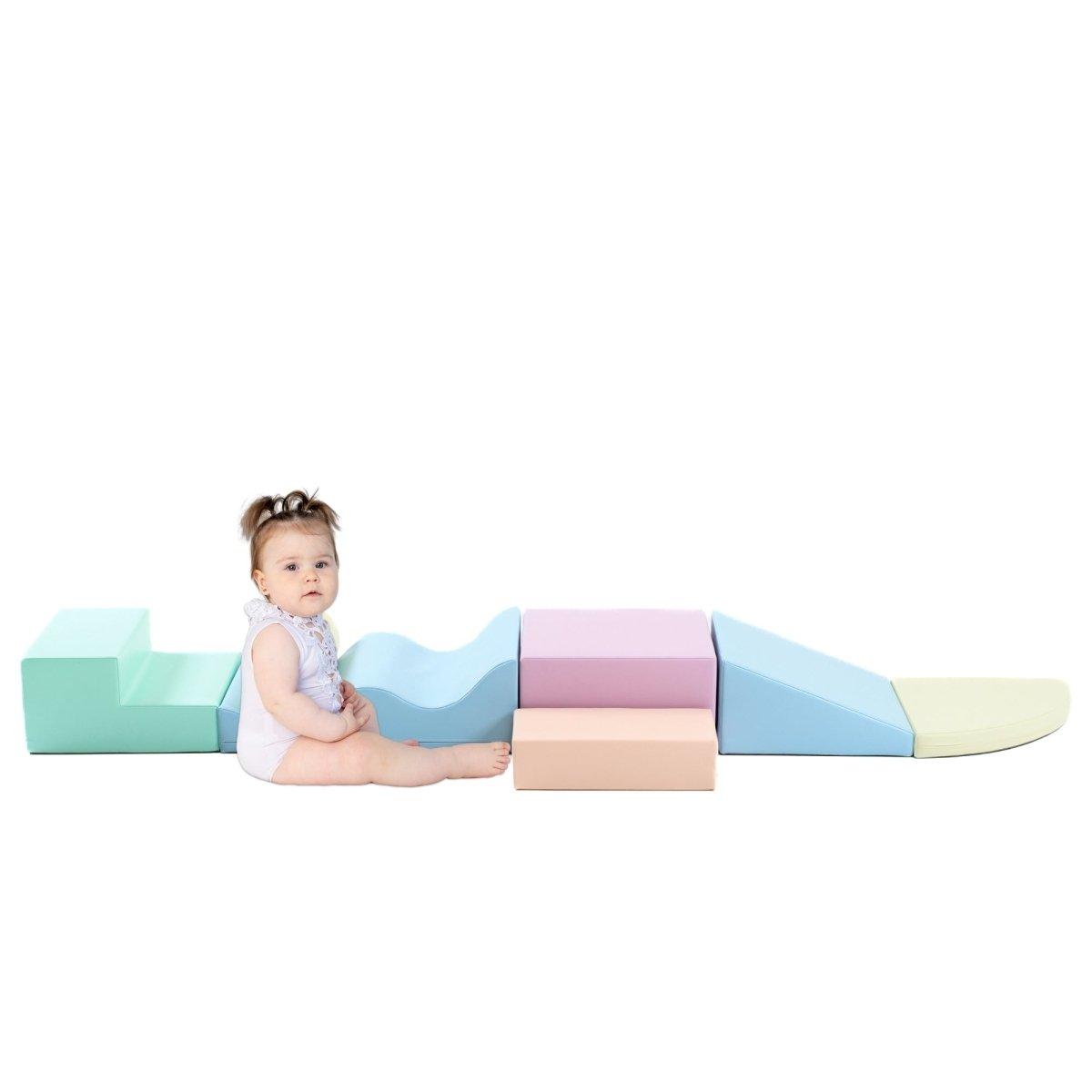 Curious baby sitting by light pastel soft play set arranged by various shapes, including wedges, steps, squares, and more