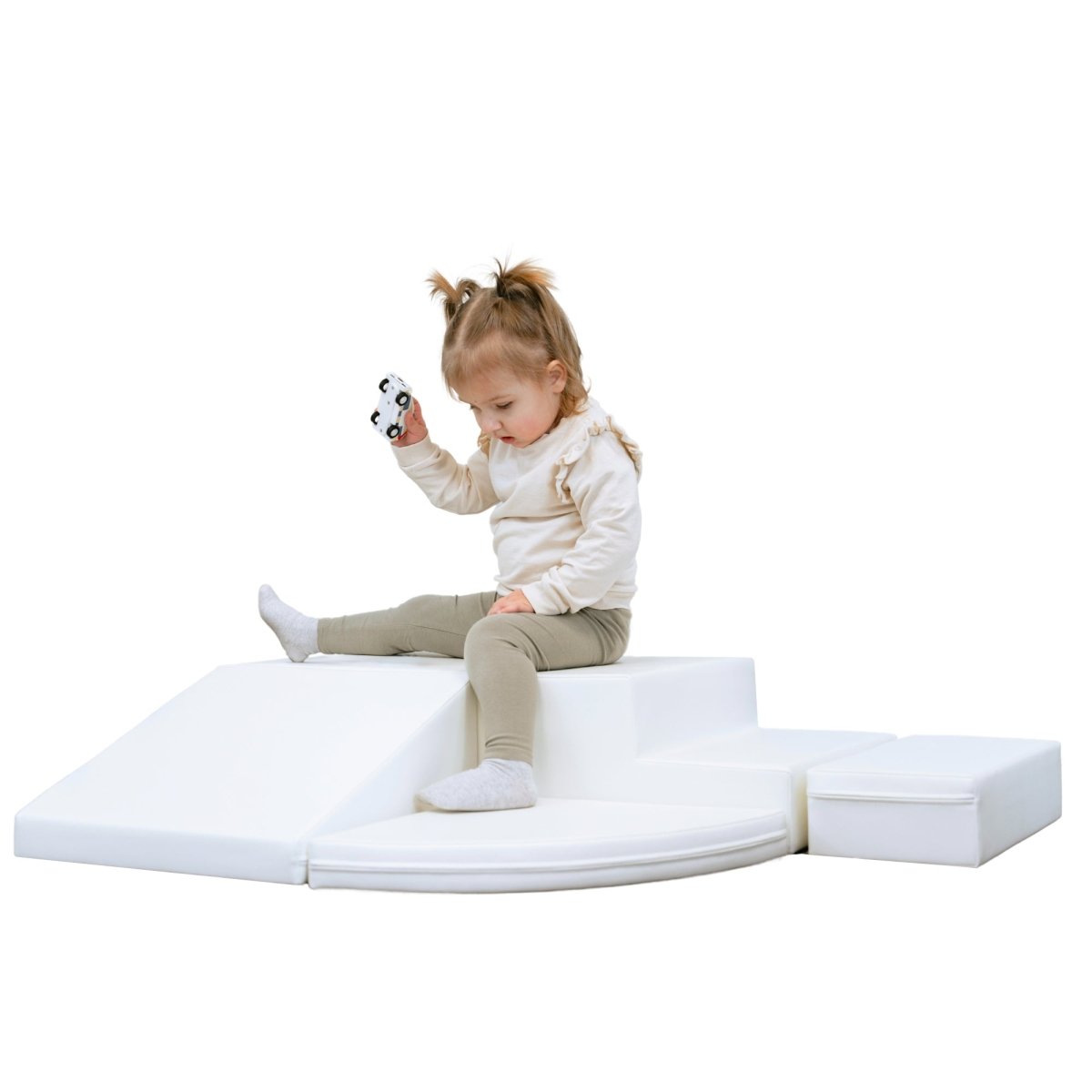 An intrigued toddler sitting on a white soft play equipment, arranged from various shapes like squares, steps, and a semicircle