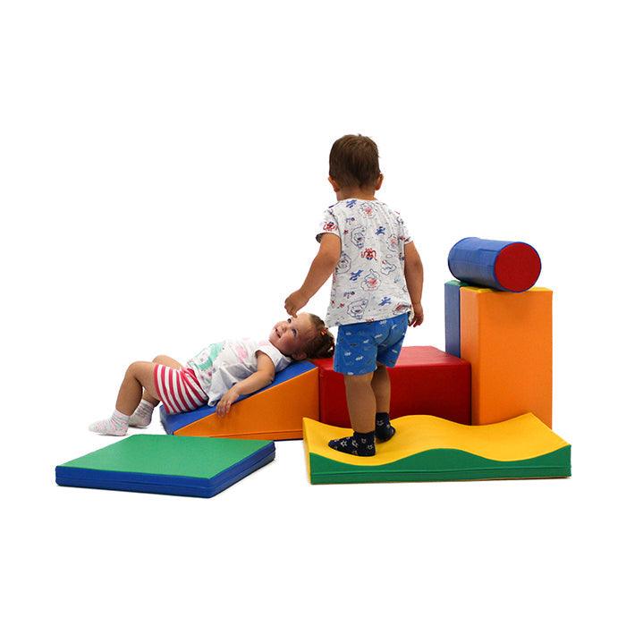 Two toddlers playing with multicolored soft play blocks, made from various shapes like wedges, squares, and cylinders