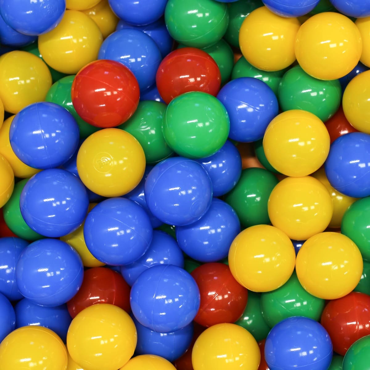 Close-up of numerous shiny multicolored plastic ball pit balls. Spheres fill the frame, reflecting light on their surfaces