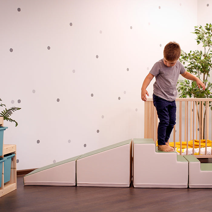 A young boy is engaging in imaginative play on a set of stairs in a child's room, promoting gross motor skill development with the IGLU Soft Play 4 Piece Soft Play Step and Slide Set - Transformer.