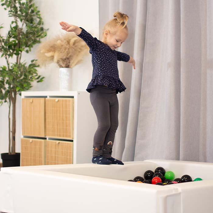A toddler girl jumping into a white foam ball pit