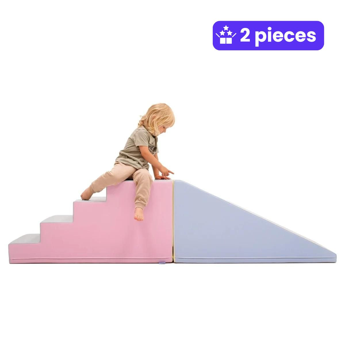 A child in beige clothes sits atop large and pink soft play steps, pointing at an adjacent light purple ramp