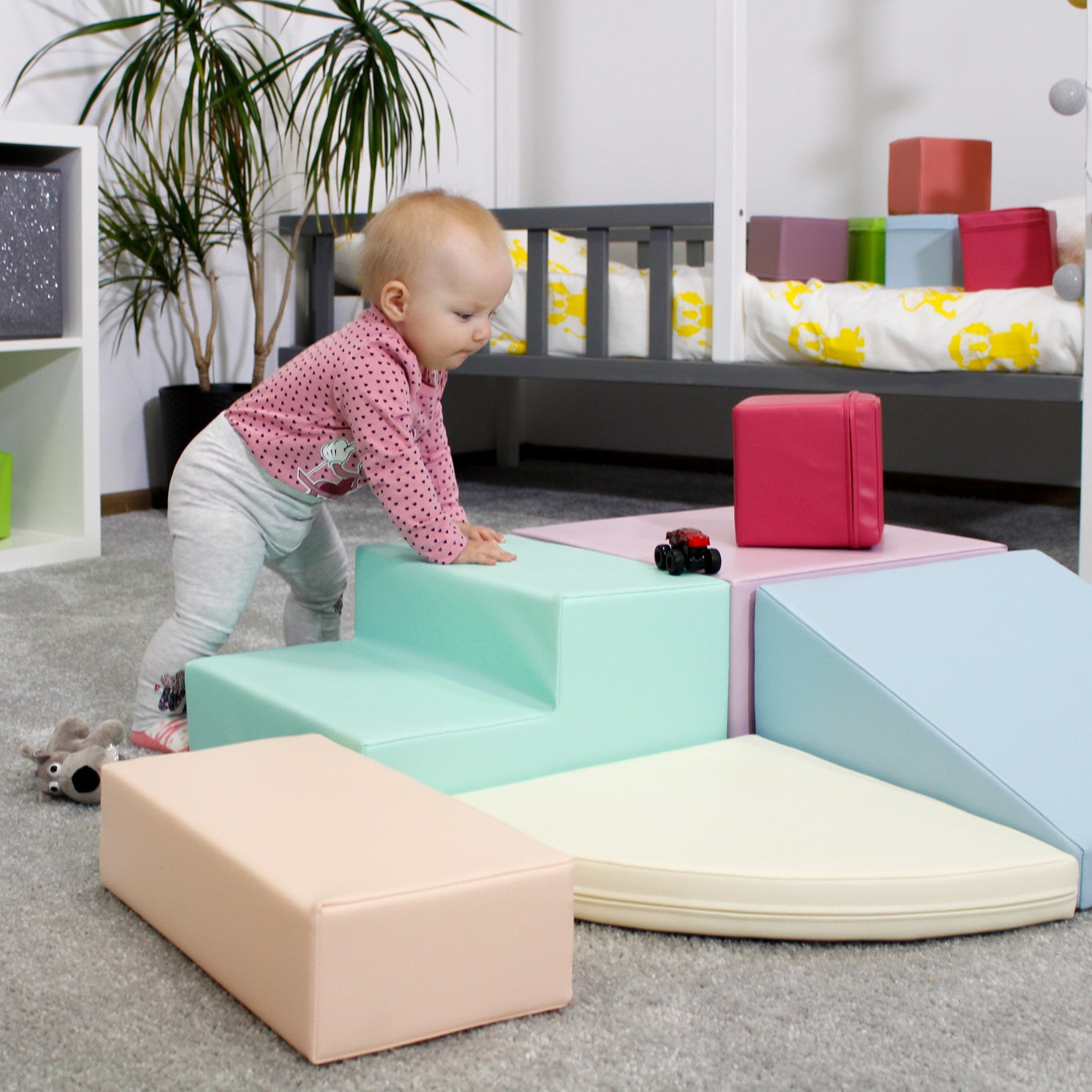 Toddler resting their arms on mint-colored steps, which are a part of a pastel soft play set located on the floor, in a room