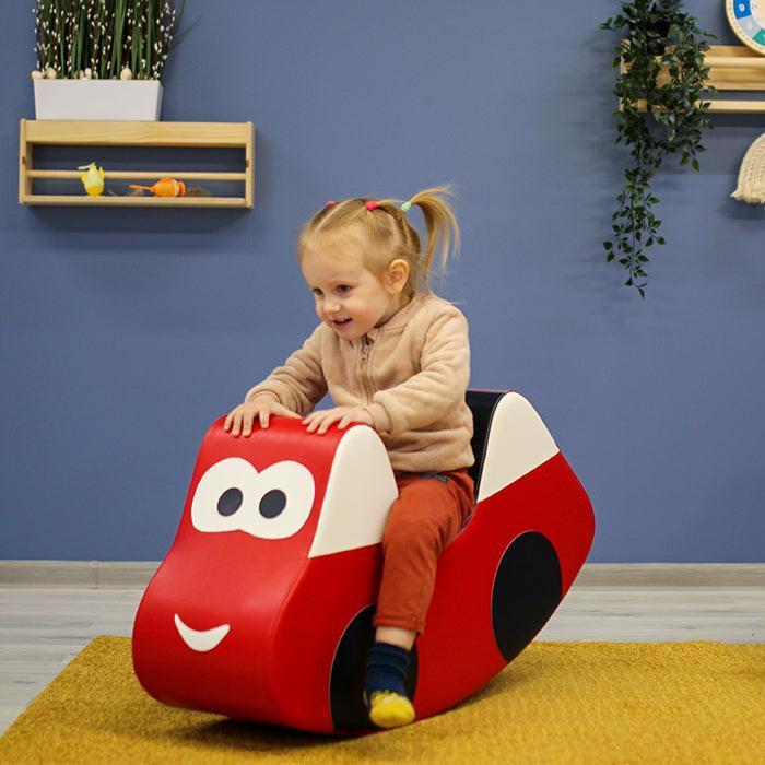 A girl rocking in a red car-like foam rocker