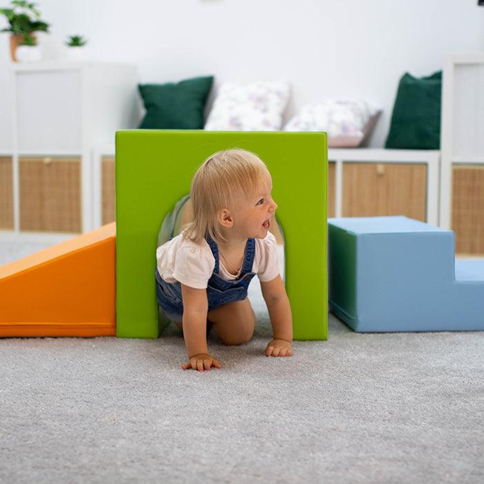 A little girl is having fun playing with the IGLU Soft Play Soft Play Set - Mini Tunnel Climber and stimulating her physical development in a room.