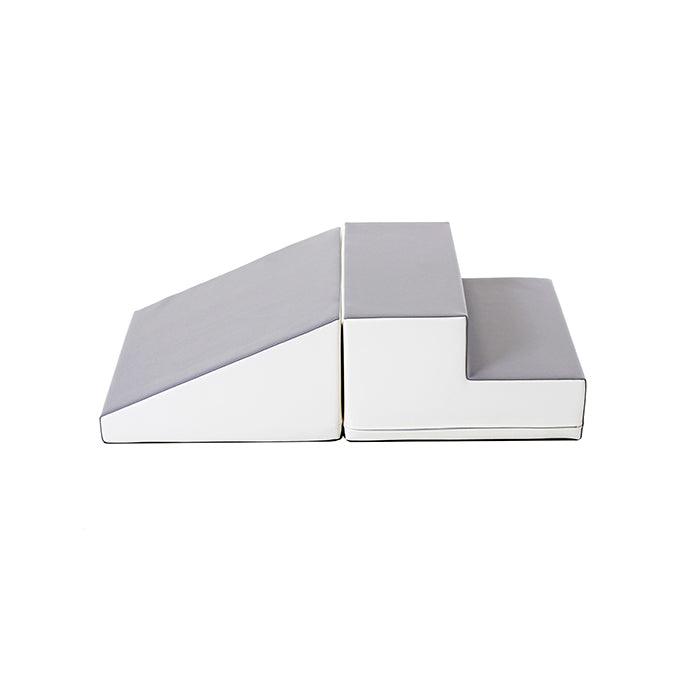 Two gray and white soft play blocks, one a ramp and the other steps, placed side by side