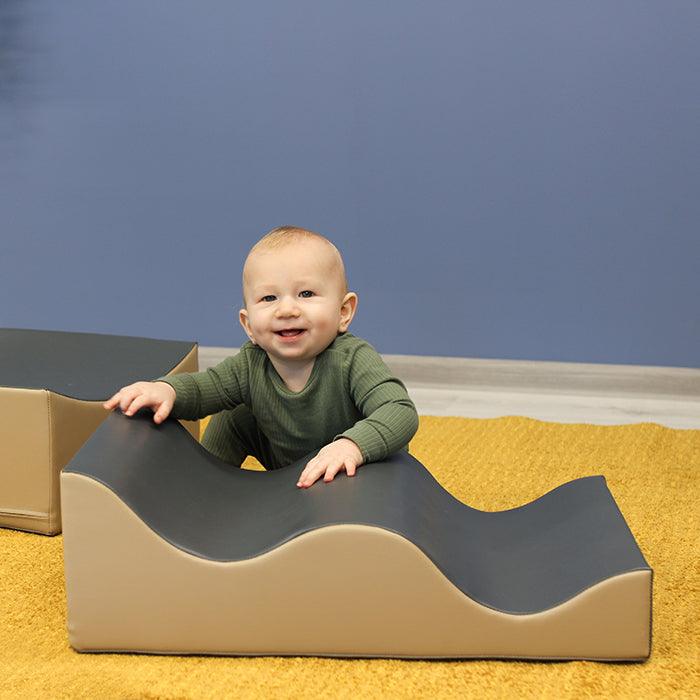 A baby is sitting on a Soft Play Set - Wave Venture by IGLU Soft Play and learning to climb.