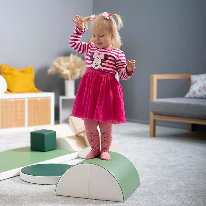 A baby girl in pink is balancing on an IGLU foam set