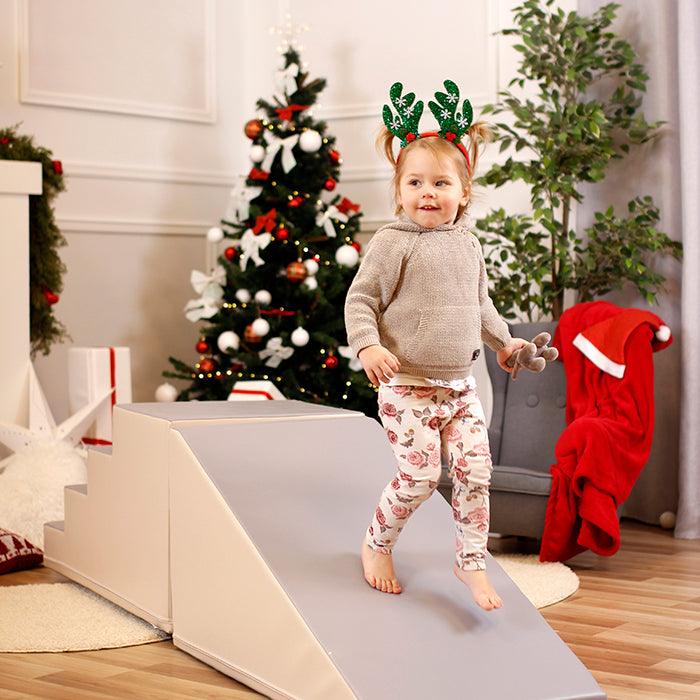A little girl is having IGLU Soft Play's Soft Play Step and Slide Set - Mega Fun Slider on a soft play ramp in front of a Christmas tree.